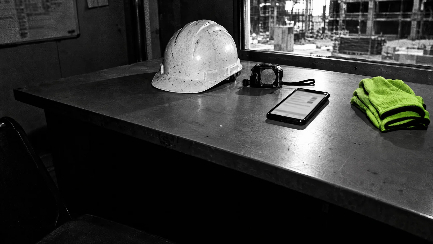 A mesa do estaleiro limpa: o capacete, o telemóvel com o registo das horas e as luvas dobradas